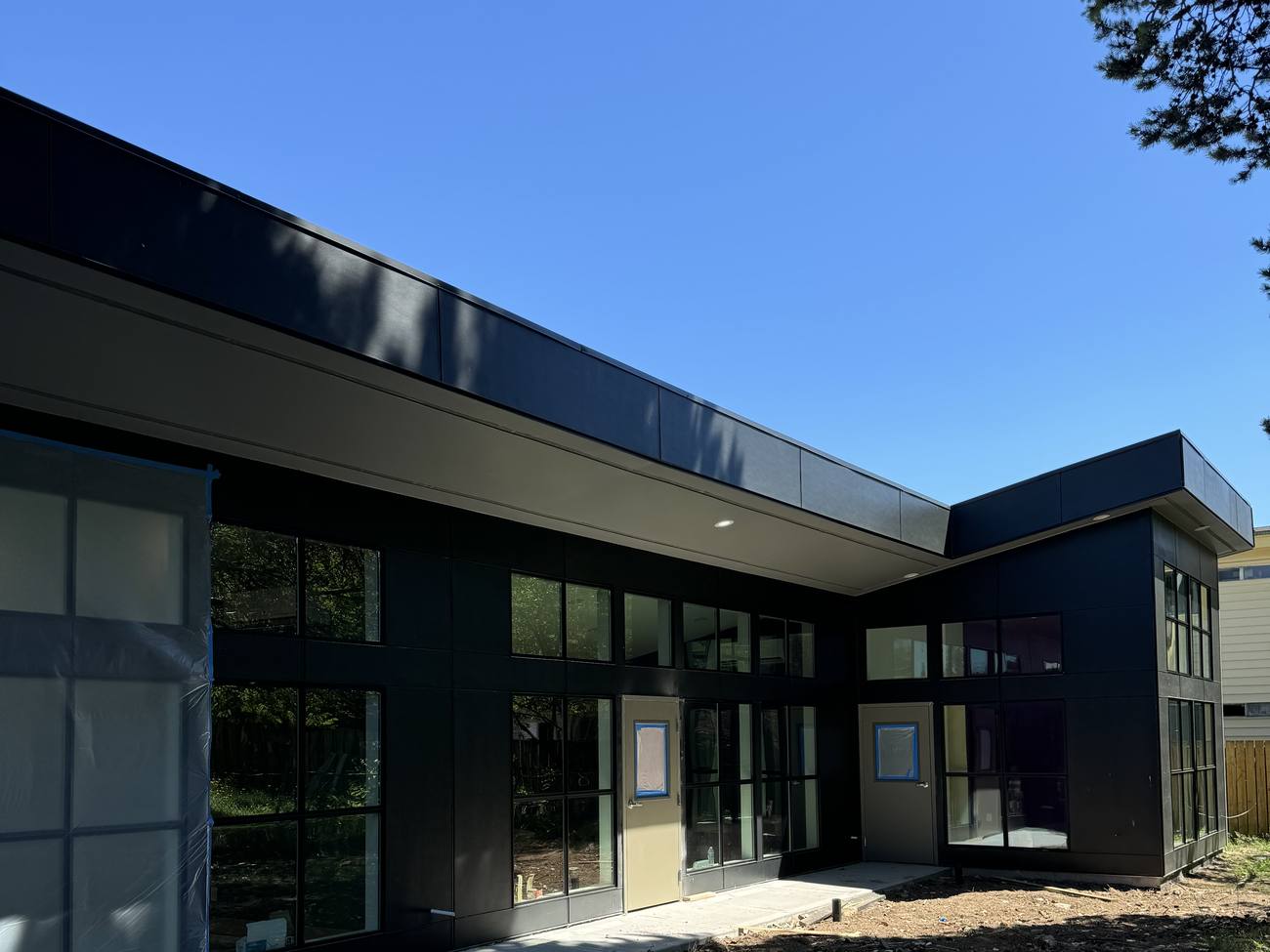 Exterior of Inspire Kids Early Learning Center: dark modern building with full-height glazing and a deep overhang under a clear blue sky
