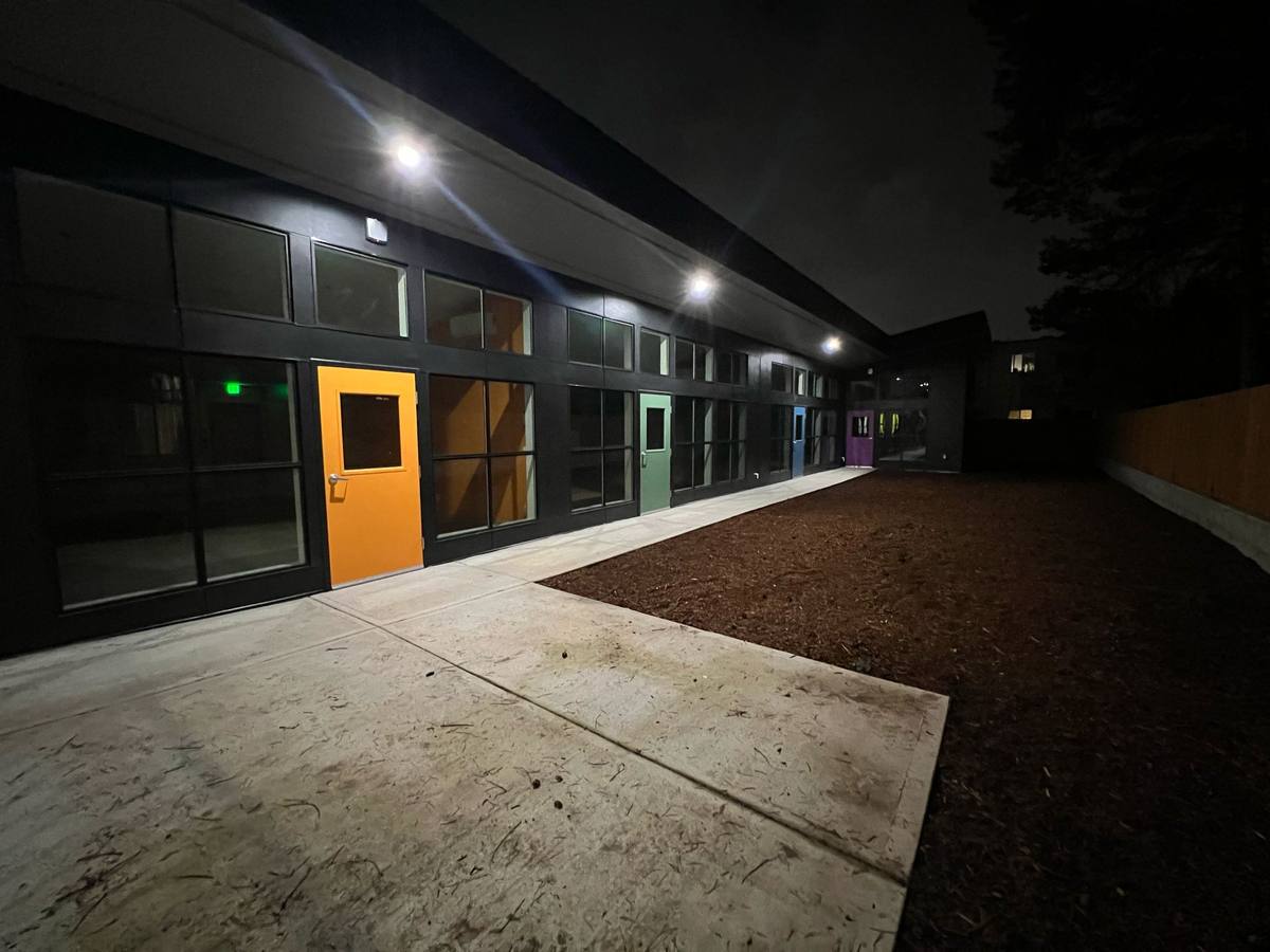 Covered exterior walkway at night with lit classroom entries and coloured doors
